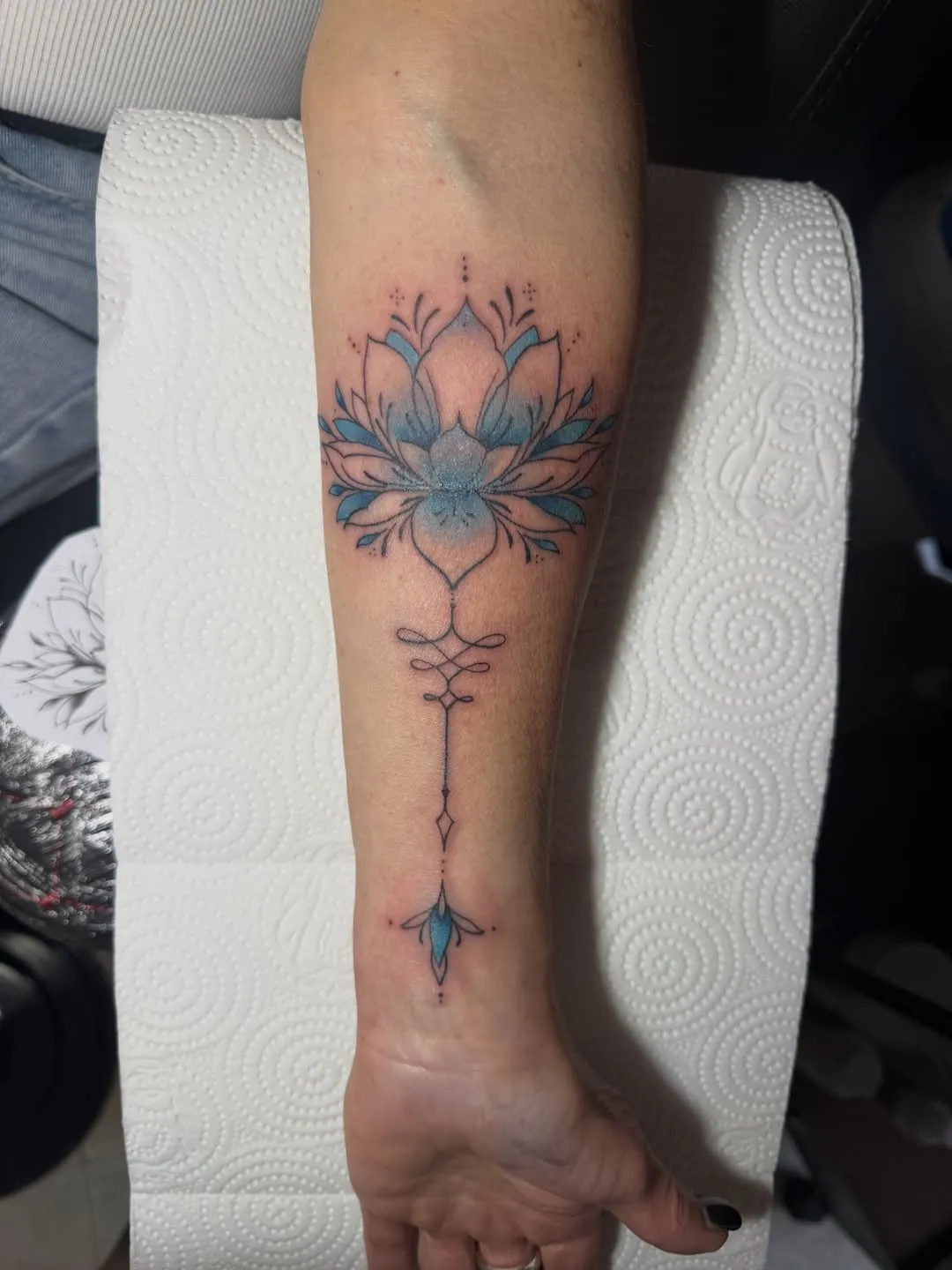 Fine line ornamental lotus tattoo with soft blue tones